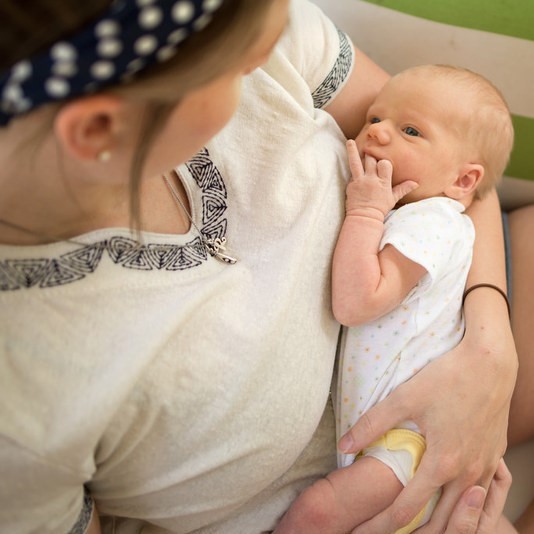 An infant looks up at its mother as she cradles the child in her arms.