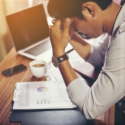 A man holds his head in frustration as he looks down at some paperwork.